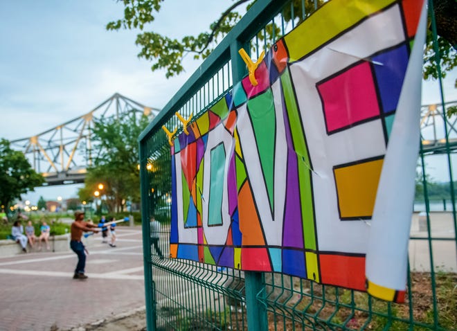 A colorful sign proclaiming "Love" hangs on a fence as enthusiastic hula-hoopers and jugglers perform during a weekly gathering of the Heart of Illinois Hoopers at the Gateway Building on the Peoria riverfront.